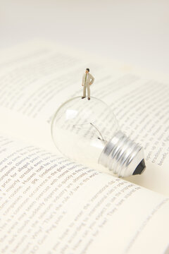 Miniature businessman on light bulb over open book representing business idea