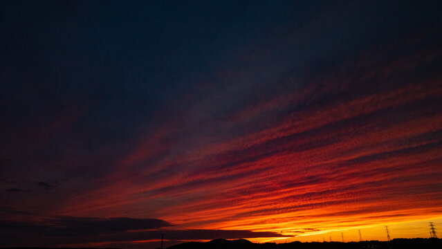 Vivid red and orange sunset over silhouetted hills and power transmission towers