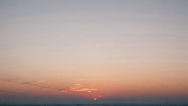 Radiant sun disk disappearing behind dark hazy mountains at dusk with soft pastel pink orange gradient sky above calm horizon