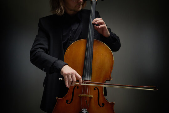 Caucasian young adult man playing cello with bow during classical music performance. Useful for concert promotion, instrumental education, symphony advertising, music school marketing