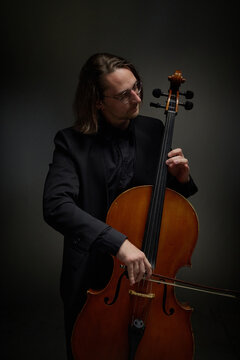 Vertical image of Caucasian young adult man playing cello during classical music performance. Content suitable for orchestra concert promotion and arts education marketing