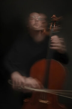 Vertical image of young adult Caucasian musician playing cello with motion blur. Concept of classical music concert, audio performance, artistic marketing