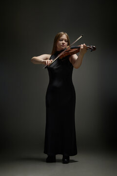 Vertical shot of young Caucasian woman playing acoustic violin during concert performance. Visual metaphor for classical music education, artistic talent, and cultural event promotion