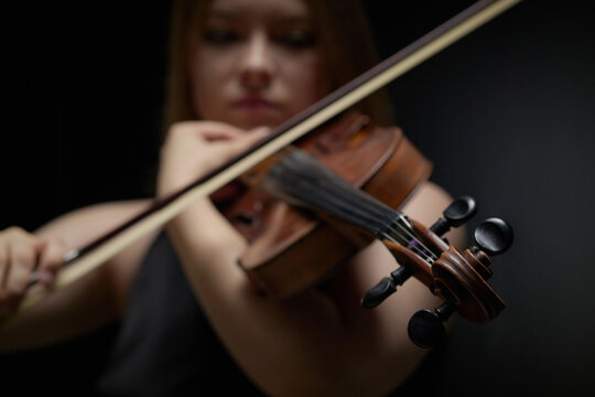 Young Caucasian woman playing violin in studio with focus on musical instrument scroll and bow. Scene ideal for classical music education campaigns and arts concert promotion
