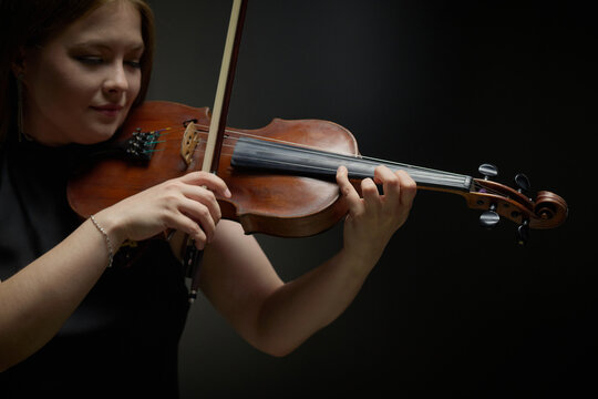 Young adult Caucasian woman playing violin during classical music performance. Image suitable for arts education, orchestra advertising, and acoustic concert promotion