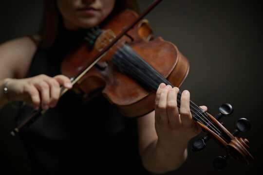 Caucasian young adult woman playing violin during classical music performance, close up shot. Useful for promoting music education, symphony orchestra events, and arts academy