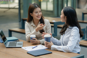 Obraz premium Two Asian businesswomen discussing app wireframe design and user interface layout on table outdoors.