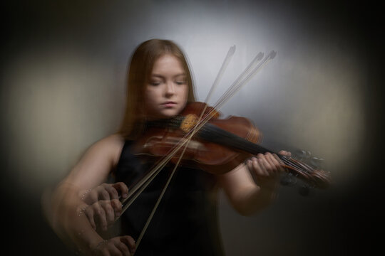 Caucasian young adult girl playing violin with motion blur effect during classical music recital rehearsal. Visual concept for music school advertising and concert promotion
