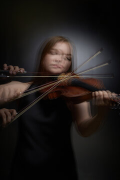 Vertical shot of young Caucasian woman playing violin with long exposure motion blur. Visual represents musical performance suitable for classical concert advertising