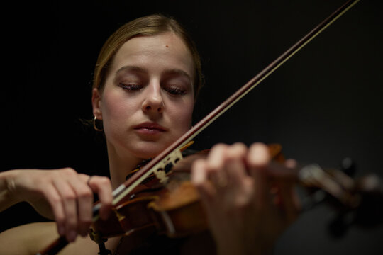 Young adult Caucasian woman playing acoustic violin with closed eyes during concert performance. Visual metaphor for music education, classical arts and cultural events promotion