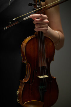 Vertical image of Caucasian young adult female musician holding wooden violin with bow. Classical string instrument performance representing arts education and concert marketing