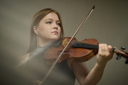Young adult Caucasian woman playing violin during classical music performance. Image suitable for arts education, concert promotion, musical theater advertising, cultural marketing