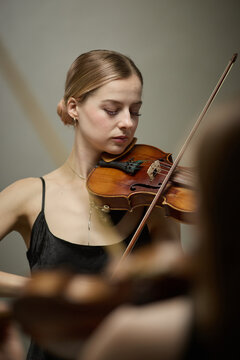 Vertical shot of young adult Caucasian woman playing violin during classical music concert rehearsal. Visual representing performing arts education and cultural event promotion
