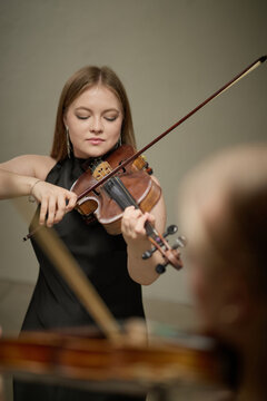 Vertical shot of young adult Caucasian woman playing violin during classical music performance rehearsal. Visual metaphor for artistic talent suitable for concert advertising