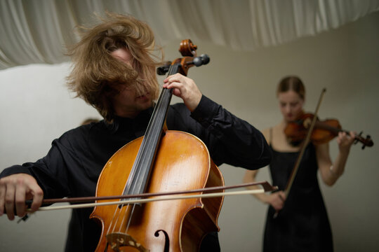 Young adult Caucasian musicians playing cello and violin during rehearsal. Concept represents acoustic performance, suitable for classical concert advertising and orchestra promotion