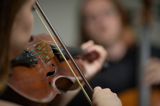 Young Caucasian woman playing violin during orchestra rehearsal in music school. Close up view highlighting classical performance for arts education and instrumental concert advertising