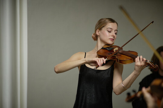 Young adult Caucasian woman playing violin during concert rehearsal. Image suitable for classical music education campaigns, orchestral performance promotion, cultural event advertising