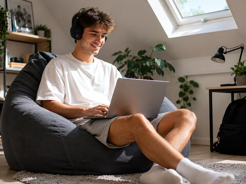 A man sits on the floor indoors, deeply focused on a laptop computer placed on his lap. A man sitting on the floor indoors.