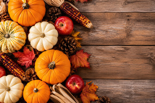 Several small pumpkins in shades of orange and cream, alongside ears of corn, are arranged on a weathered wooden surface.