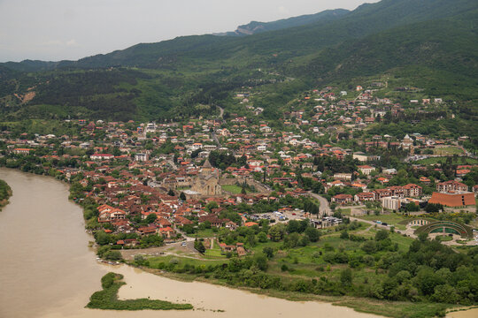 Mtskheta town and Svetitskhoveli cathedral viewed from Jvari monastery, showcasing the historical settlement nestled between the converging Kura and Aragvi rivers amidst the green caucasus mountains