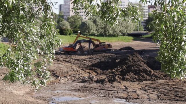Excavator operates on a muddy construction site amid piles of earth and visible tire tracks