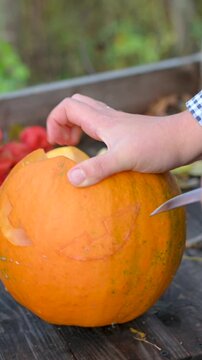 Vertical video: Close-up of human hands carving a spooky scary face on a Halloween pumpkin with a knife. DIY holiday decoration process. 9:16 format.