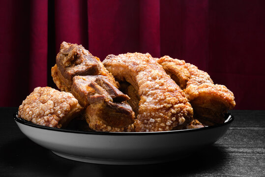 Chicharrones on a Plate on Black Wooden Table with Red Curtain