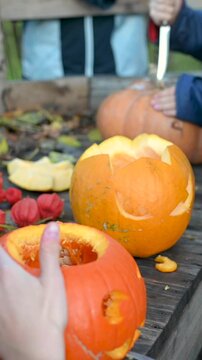 Vertical video: Close-up of human hands carving a spooky scary face on a Halloween pumpkin with a knife. DIY holiday decoration process. 9:16 format.
