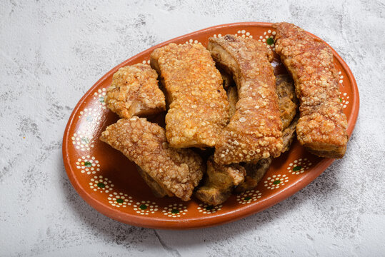 Large Crispy Chicharrones on Clay Plate Over Cement Surface