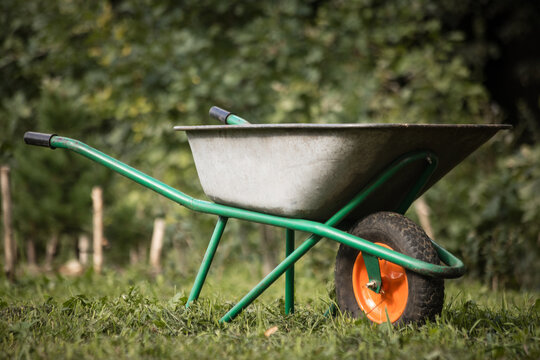 Garden scene with  wheelbarrow and wooden posts in a grassy field, outdoor work area.