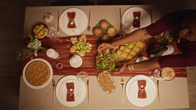 African American woman placing fresh salad bowl on Thanksgiving dinner table from top view. Clip works for holiday food advertising, festive catering campaigns, autumn seasonal promotions