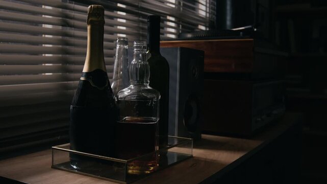 Glass alcohol bottles, whiskey decanter, and champagne bottle standing on tray indoors. Visual metaphor suited for substance abuse awareness, alcoholism recovery campaigns, and mental health media