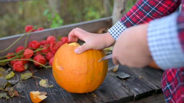 Close-up of human hands carving a spooky scary face on a Halloween pumpkin with a knife. DIY holiday decoration process.