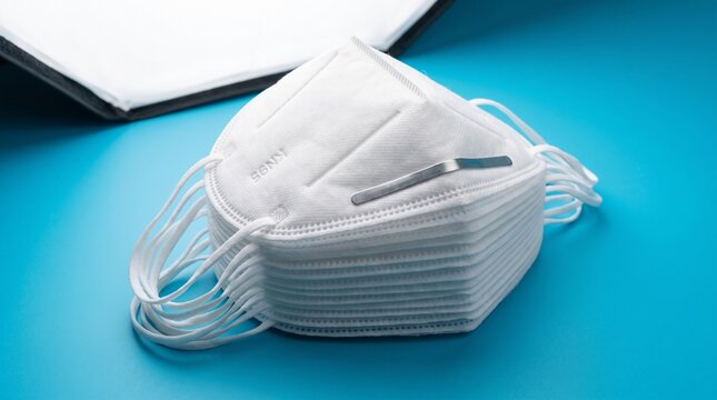 Stack of white KN95 protective face masks on blue background with open binder, medical and healthcare concept