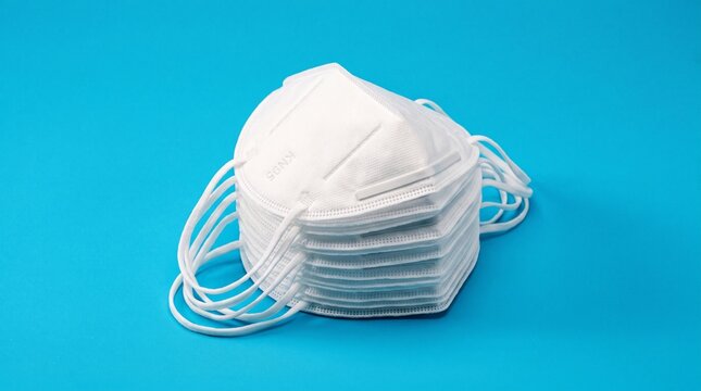 Stack of white KN95 protective face masks on bright blue background, personal protective equipment concept