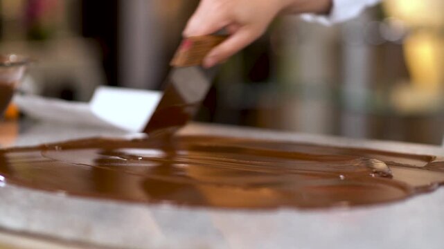 Professional pastry chef tempering melted milk chocolate on marble table surface in kitchen.