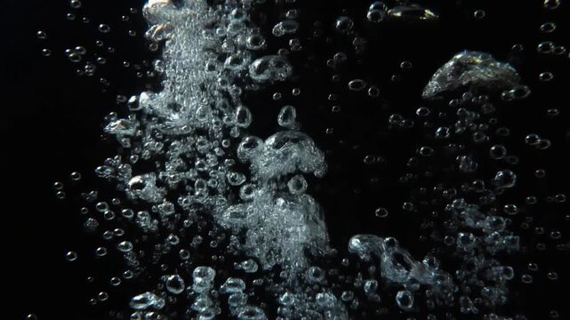Crystal clear air bubbles rising underwater on a black background