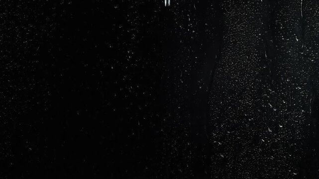 Raindrops flowing down a glass window at night with dark background