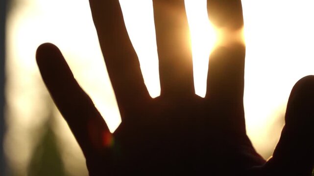 Close up hand blocking golden sunlight with bright lens flare through fingers