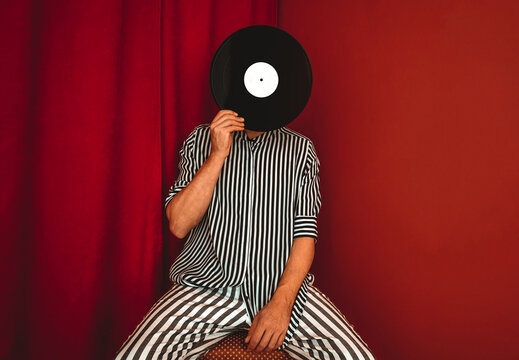 Person in striped shirt holding vinyl record in front of face indoors