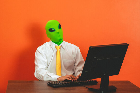 Man wearing an alien mask works on a computer at the office