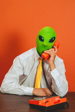 Man in alien mask talks on retro telephone at the office