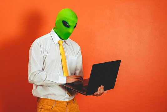 Man in alien mask typing on laptop in orange studio