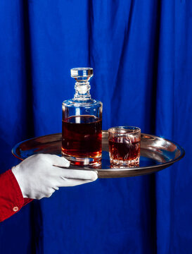 Waiter holding a silver tray with whiskey decanter and glass