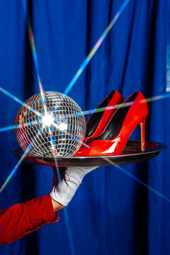 A male waiter holds a tray with a discoball and a red shoe indoors