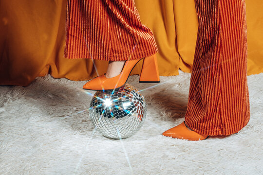 Person in orange bell bottom pant steps on a disco ball indoors