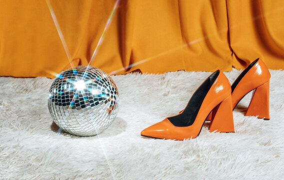 A fluffy carpet holds a shiny disco ball and an orange shoe