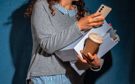 Overwhelmed woman holds box and coffee while using smartphone