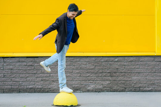 Smiling businessman balancing on a yellow bollard outdoors