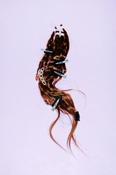 A brown hair extension features pearl clips on a lilac background